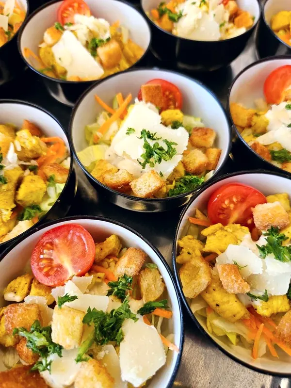 Caesarsalade met kip, croutons, Parmezaan en een kerstomaatje in bakjes om mee te nemen.
