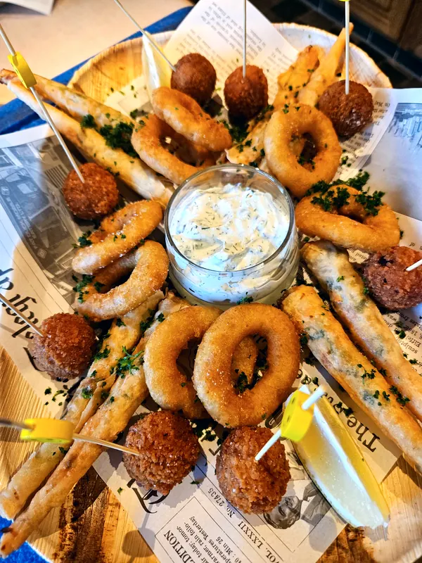Het bordje van de visser: gefrituurde inktvisringen, vissticks en kroketjes op krantenpapier, met citroen en een potje tartaar.