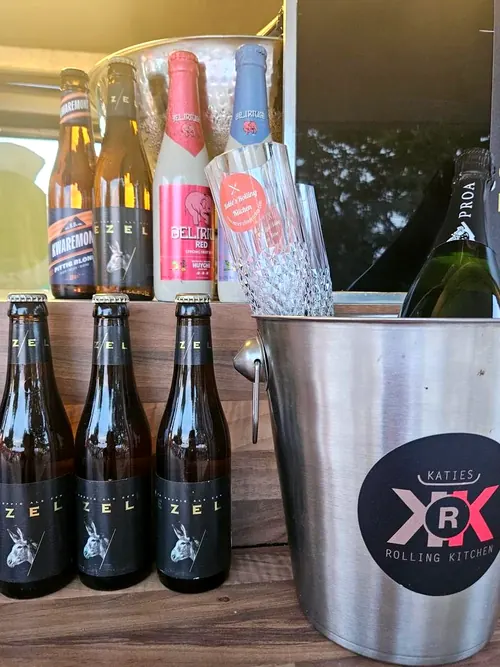 Flesjes Kwaremont, Ezel, Delirium Red en Delirium Tremens naast een ijsemmer met het logo van Katie's Rolling Kitchen en een fles cava Proa.