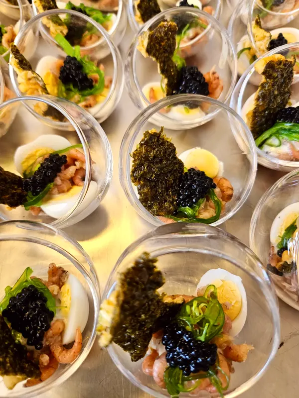 Glaasjes met grijze garnalen, een half kwarteleitje, zeewiersalade, kaviaar en een krokant zeewierchipje.