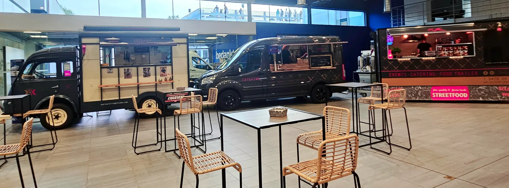 De Goelette, de Transit en de trailer samen op een event in een showroom, met statafels en rieten stoelen ervoor.